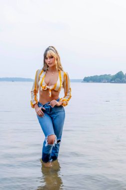 Işıl ışıl, koyu kahverengi ve karamel renkli iki tonlu saçları olan Meksikalı genç bir Amerikalı kadın sıcak bir şekilde gülümsüyor. Berrak bir göl kenarında güneşli bir yaz gününün tadını çıkarıyor. Etrafı yemyeşil ve ışıldayan suyla çevrili..