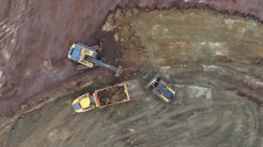 Hareketli bir inşaat alanının hava görüntüsü, toprağı şekillendiren buldozerleri, kamyonları ve not verme ekipmanlarını gösteriyor. Toprak yollar, temizlenmiş alanlar ve dağınık malzemeler..