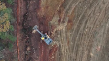 Hareketli bir inşaat alanının hava görüntüsü, toprağı şekillendiren buldozerleri, kamyonları ve not verme ekipmanlarını gösteriyor. Toprak yollar, temizlenmiş alanlar ve dağınık malzemeler..
