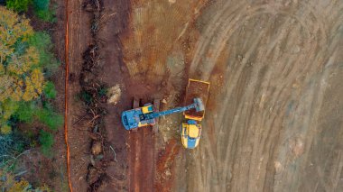 Hareketli bir inşaat alanının hava görüntüsü, toprağı şekillendiren buldozerleri, kamyonları ve not verme ekipmanlarını gösteriyor. Toprak yollar, temizlenmiş alanlar ve dağınık malzemeler.