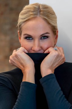 Güzel sarışın bir kadın kendine güvenerek ayakta duruyor, ışıl ışıl gülüşü ve kendine güvenen tavırları zarafet saçıyor. Zarif duruşu çekiciliğini vurguluyor, zamansız güzellik ve kendine güvenin görüntüsünü yaratıyor..