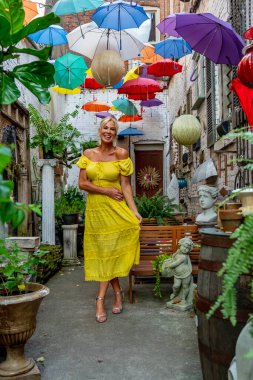 Güzel sarışın bir kadın zarif bir şekilde canlı ve renkli şemsiyelerin altında geziniyor. Neşeli ifadesi ve hafif adımları renkli sahnenin neşeli, canlı atmosferine ekleniyor..