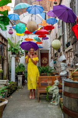 Güzel sarışın bir kadın zarif bir şekilde canlı ve renkli şemsiyelerin altında geziniyor. Neşeli ifadesi ve hafif adımları renkli sahnenin neşeli, canlı atmosferine ekleniyor..