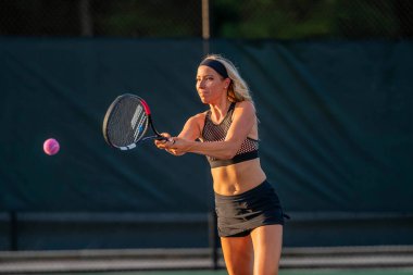Enerjiyle parlayan genç ve güzel bir atlet, parlak yaz güneşi altında yoğun bir tenis turu atıyor. Onun hızlı hareketleri ve odaklanmış bakışları zarafeti, gücü ve oyuna olan tutkusunu simgeliyor..