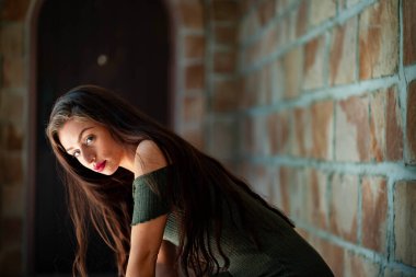 Çekici genç bir esmer, dalgalı beyaz bir bahar elbisesi içinde, saçları dalgalar halinde dalgalanırken dışarıda poz veriyor. Gülümsüyor, uzun ve sert bir kışın ardından baharın yumuşak sıcağında güneşleniyor..