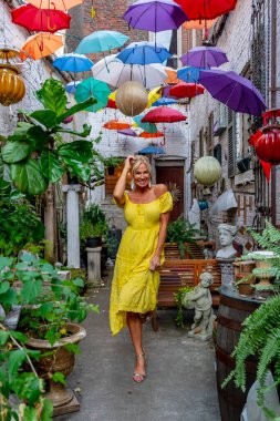 A beautiful blonde woman strolls gracefully beneath a canopy of vibrant, colorful umbrellas. Her joyful expression and light steps add to the playful, lively atmosphere of the colorful scene. clipart