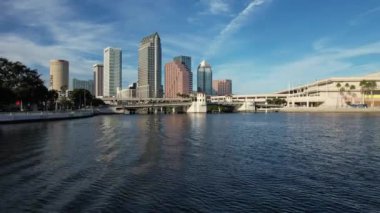 Tampa, Florida 'nın hava manzarası modern yüksek binalarla dolu canlı bir ufuk çizgisi, şehir merkezinden geçen ikonik Hillsborough Nehri, Tampa Körfezi boyunca geniş deniz kenarları ve yemyeşil noktalı kentsel alanlar gösteriyor..
