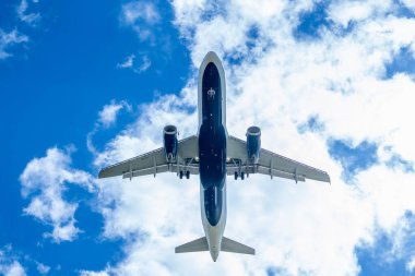 Şık bir ticari jet, hareketli bir havaalanına yaklaşırken kanatlarını, yumuşak, ince bulutlarla benekli canlı mavi bir gökyüzünün arka planına sabitler ve pürüzsüz bir iniş için hazır hale getirir..