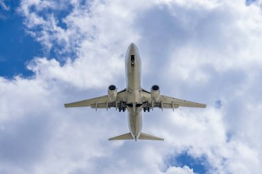 Şık bir ticari jet, hareketli bir havaalanına yaklaşırken kanatlarını, yumuşak, ince bulutlarla benekli canlı mavi bir gökyüzünün arka planına sabitler ve pürüzsüz bir iniş için hazır hale getirir..