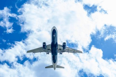 Şık bir ticari jet, hareketli bir havaalanına yaklaşırken kanatlarını, yumuşak, ince bulutlarla benekli canlı mavi bir gökyüzünün arka planına sabitler ve pürüzsüz bir iniş için hazır hale getirir..