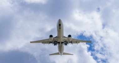 Şık bir ticari jet, hareketli bir havaalanına yaklaşırken kanatlarını, yumuşak, ince bulutlarla benekli canlı mavi bir gökyüzünün arka planına sabitler ve pürüzsüz bir iniş için hazır hale getirir..