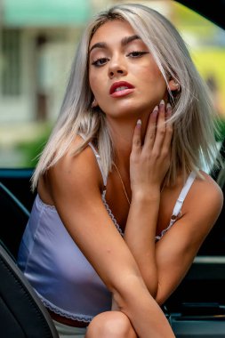 Genç, güzel bir kadın zarif bir şekilde arabada oturuyor. Rüzgâr saçlarını dalgalandırıyor dışarı bakarken, kırsal bir macerada dolaşma arzusunu somutlaştırıyor..