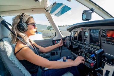 A young woman pilot diligently performs pre-flight checks beside her general aviation aircraft, under clear blue skies, embodying precision and passion on a perfect flying day. clipart