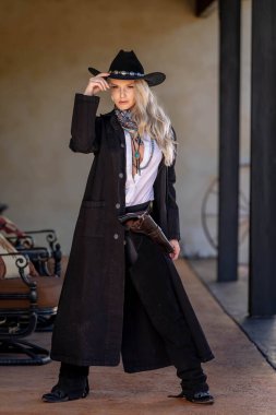 Klasik kovboy kıyafetli, kendine güvenen, güzel, sarışın bir kadın uzun boylu, kalçasında bir tabanca ve omzunda bir tüfekle poz veriyor. Gülüşü enerji ve korkusuz cazibe saçıyor..