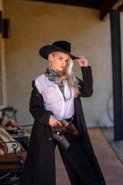 Klasik kovboy kıyafetli, kendine güvenen, güzel, sarışın bir kadın uzun boylu, kalçasında bir tabanca ve omzunda bir tüfekle poz veriyor. Gülüşü enerji ve korkusuz cazibe saçıyor..