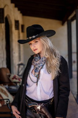 Klasik kovboy kıyafetli, kendine güvenen, güzel, sarışın bir kadın uzun boylu, kalçasında bir tabanca ve omzunda bir tüfekle poz veriyor. Gülüşü enerji ve korkusuz cazibe saçıyor..