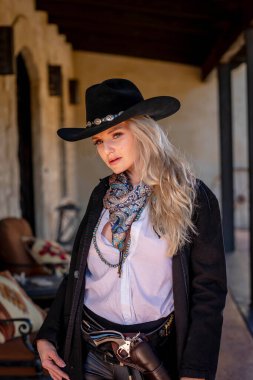 Klasik kovboy kıyafetli, kendine güvenen, güzel, sarışın bir kadın uzun boylu, kalçasında bir tabanca ve omzunda bir tüfekle poz veriyor. Gülüşü enerji ve korkusuz cazibe saçıyor..