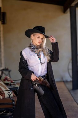 Klasik kovboy kıyafetli, kendine güvenen, güzel, sarışın bir kadın uzun boylu, kalçasında bir tabanca ve omzunda bir tüfekle poz veriyor. Gülüşü enerji ve korkusuz cazibe saçıyor..