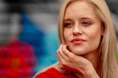 Güzel sarışın bir kadın, şık bahar kıyafetlerini göstererek kameraya neşe içinde poz veriyor. Parlak bir gülümseme ve neşeli tavırlarıyla yaklaşan muhteşem havayı kucaklayarak mutluluk saçıyor..