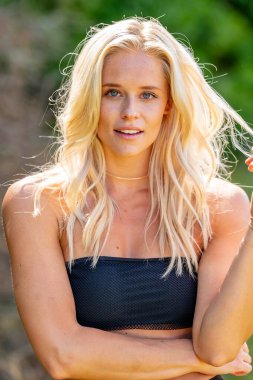 Büyüleyici bir sarışın, narin iç çamaşırlarıyla yemyeşil tarlalar ve çiçek açan çiçeklerin arasında poz vererek baharın sıcağında güneşleniyor. Doğanın güzelliğini kusursuz bir şekilde kucaklayan neşe ve zarafet saçıyor..