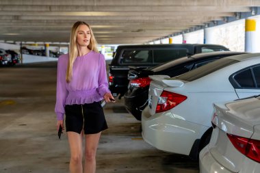 Güzel sarışın bir kadın, iş kıyafeti giymiş, loş bir otoparkta arabasına doğru gidiyor. Yorgun ama sakin bir şekilde uzun ve verimli bir iş gününden sonra kapıyı açar..