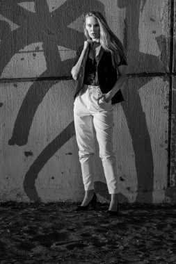 Çekici genç sarışın bir kadın zarif bir şekilde poz verir, batan güneşin sıcacık parıltısıyla yıkanır. Şehir arkaplanı onun tarzını geliştirir. Güzellik ve şehir cazibesinin büyüleyici bir karışımını yaratır..