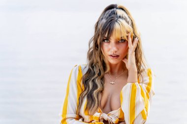 Işıl ışıl, koyu kahverengi ve karamel renkli iki tonlu saçları olan Meksikalı genç bir Amerikalı kadın sıcak bir şekilde gülümsüyor. Berrak bir göl kenarında güneşli bir yaz gününün tadını çıkarıyor. Etrafı yemyeşil ve ışıldayan suyla çevrili..