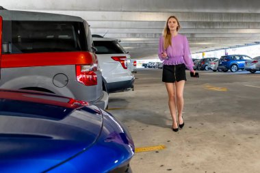 Güzel sarışın bir kadın, iş kıyafeti giymiş, loş bir otoparkta arabasına doğru gidiyor. Yorgun ama sakin bir şekilde uzun ve verimli bir iş gününden sonra kapıyı açar..