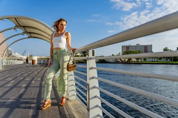 Çekici genç bir sarışın model şehir merkezinde poz veriyor. Şık yaz kıyafeti parlak mavi gökyüzüne tamamen zıt düşüyor. Kendine güveni tam, sıcaklığı ve zahmetsizliği yayıyor..