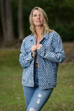 Güzel bir sarışın manken yaz sonu güneşinin tadını çıkarıyor. Bereketli yeşillik ve yumuşak güneş ışığıyla çevrili, o, sıcaklığı ve zarafeti serin, altın ışıkta yayar..