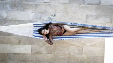 Muhteşem bir kadın hamakta dinleniyor, yavaşça Karayip güneşinin altında sallanıyor. Bereketli doğayla çevrili, huzurlu, tembel bir günün tadını çıkarıyor, tropikal tatilinin huzurlu güzelliğini kucaklıyor..