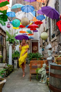 Güzel sarışın bir kadın zarif bir şekilde canlı ve renkli şemsiyelerin altında geziniyor. Neşeli ifadesi ve hafif adımları renkli sahnenin neşeli, canlı atmosferine ekleniyor..