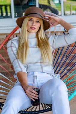 Şık giyinmiş, göz kamaştırıcı genç bir sarışın açık hava alışveriş merkezinde gazoz içiyor. Güneş onu sıcağa boğuyor. O, canlı ve açık havada esen enerjiyi ve rahatlatıcı esintiyi içine çekerken..