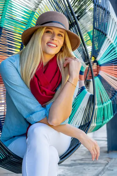 Sarışın, güzel bir kadın yerel bir alışveriş merkezinde geziniyor, açık havayı seyrediyor. Rahat bir gülümseme ile, canlı ortamın canlı atmosferinin ve sıcak güneşin tadını çıkarıyor..