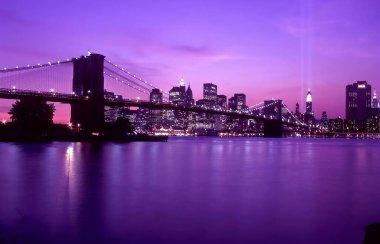 2003 New York silueti alacakaranlıkta, kulelerin bir zamanlar durduğu yerde ikiz ışık huzmeleri gibi yumuşak bir şekilde parlıyor. Hudson, sakin şehir manzarasında kasvetli ama birleşmiş bir ruhu yansıtıyor..
