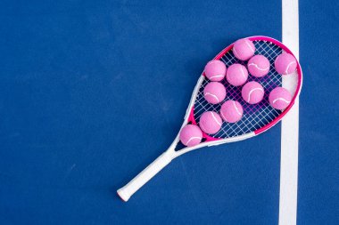 Tenis raketi taban çizgisinde uzanır, güneş ışığıyla kavranır, parlak tenis topları onun yanında dinlenir, kort boyunca uzun gölgeler bırakır sessiz bir yoğunluk anında.