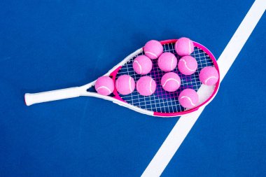 Tenis raketi taban çizgisinde uzanır, güneş ışığıyla kavranır, parlak tenis topları onun yanında dinlenir, kort boyunca uzun gölgeler bırakır sessiz bir yoğunluk anında.