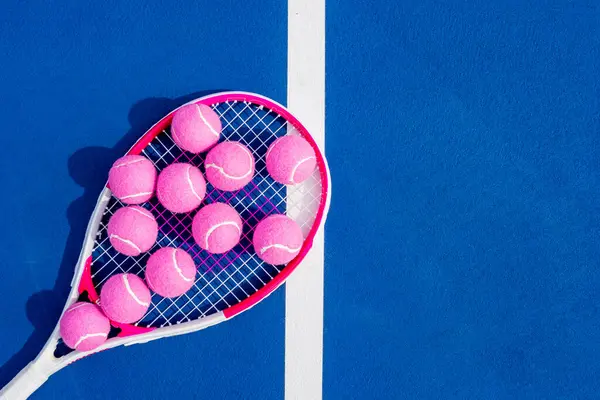 Tenis raketi taban çizgisinde uzanır, güneş ışığıyla kavranır, parlak tenis topları onun yanında dinlenir, kort boyunca uzun gölgeler bırakır sessiz bir yoğunluk anında.