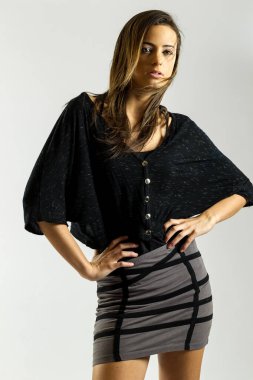 Genç esmer bir manken kameraya kendine güvenen bir poz veriyor. Temiz bir stüdyo ortamında, beyaz bir arka planla çerçevelenmiş, tarzını, duruşunu ve modern zarafetini ön plana çıkarıyor..