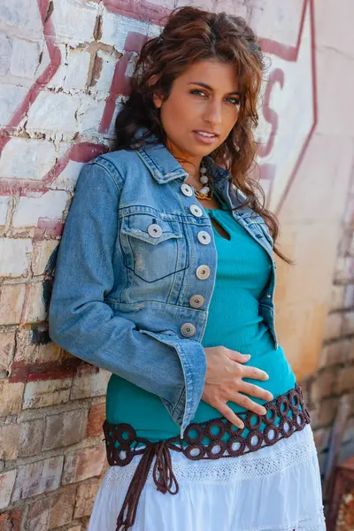 Çarpıcı genç bir melez ırk modeli, şehir ortamında kendine güvenen bir poz veriyor. Güneş ışığı, duvarların, sokak sanatının ve şehir enerjisinin arka planına vurgu yapıyor..