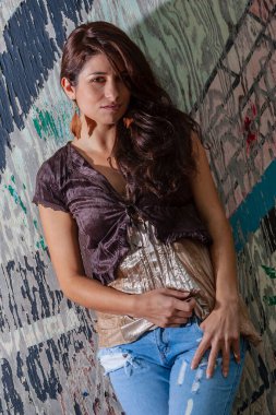 Çarpıcı genç bir melez ırk modeli, şehir ortamında kendine güvenen bir poz veriyor. Güneş ışığı, duvarların, sokak sanatının ve şehir enerjisinin arka planına vurgu yapıyor..