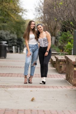 İki genç kadın yerel bir parkta birlikte gülüyor, ılık bahar havasının tadını çıkarıyorlar. Yeşillik ve günışığıyla çevrelenmiş, dostluk ve barış dolu neşeli ve tasasız bir anı paylaşıyorlar..