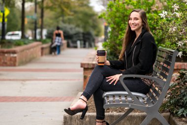 Genç, güzel bir kadın parkta oturur, kahvesini yudumlar ve bahar havasında sırılsıklam olur. Çiçekler ve ılık gün ışığıyla çevrili sakin ve huzurlu bir dinlenme anının tadını çıkarıyor..