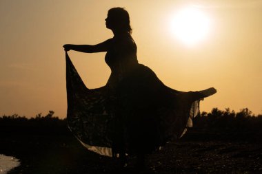 Gün batımında dans eden güzel bir kadının silueti.