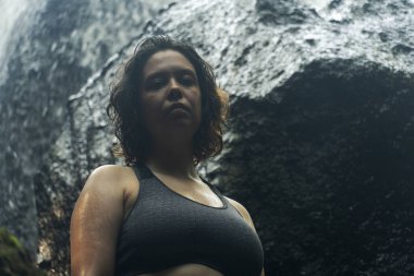 Şelalede poz veren spor giyimli genç bir kadın.