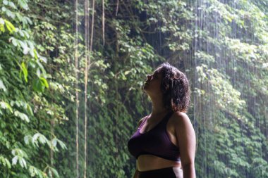 Spor kıyafetli genç bir kadın doğa manzarasında şelaleye, Bali 'ye, Endonezya' ya bakıyor..