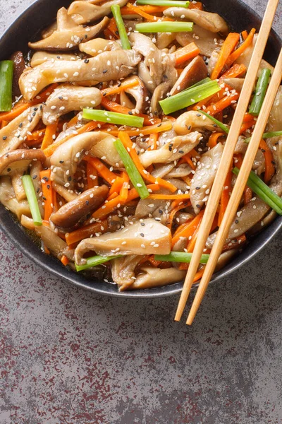 Healthy Stir-fry with shiitake and oyster mushrooms, carrots, soy sauce, sesame seeds, garlic and green onions closeup in the plate on the table. Vertical top view from abov