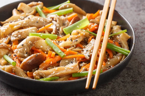 stir-fry with Shiitake and oyster mushrooms, spices, hot peppers, dark soy sauce, carrot and green onions closeup in the plate on the table. Horizonta