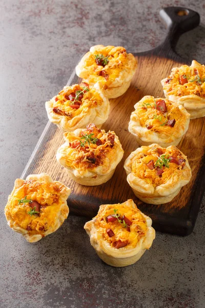 stock image Freshly baked puff pastry cups stuffed with eggs, cheese and ham close-up on a wooden board on the table. Vertica