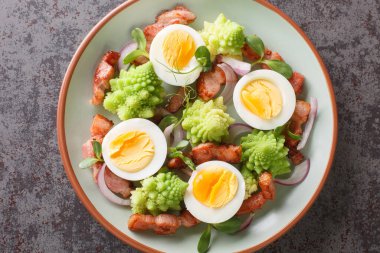 Romanesco lahana salatası, domuz pastırması, haşlanmış yumurta, kırmızı soğan ve mikro yeşiller masanın üstünde. Yukarıdan yatay üst görünüm